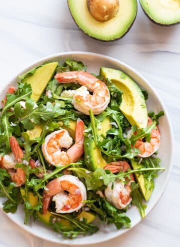 close up view of prawn and avocado salad on white plate, with halved avocado in background