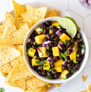 top down view of black bean mango salsa with corn chips on white tile background