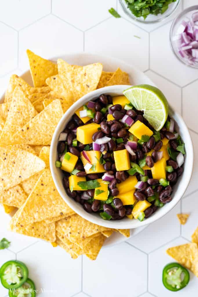 top down view of black bean mango salsa with corn chips on white tile background