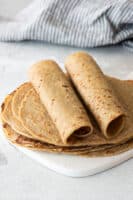 two quinoa tortillas rolled up on top of flat tortillas on gray background