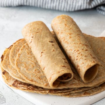 two quinoa tortillas rolled up on top of flat tortillas on gray background