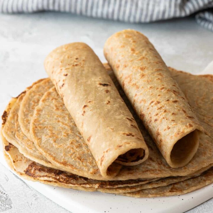 two quinoa tortillas rolled up on top of flat tortillas on gray background