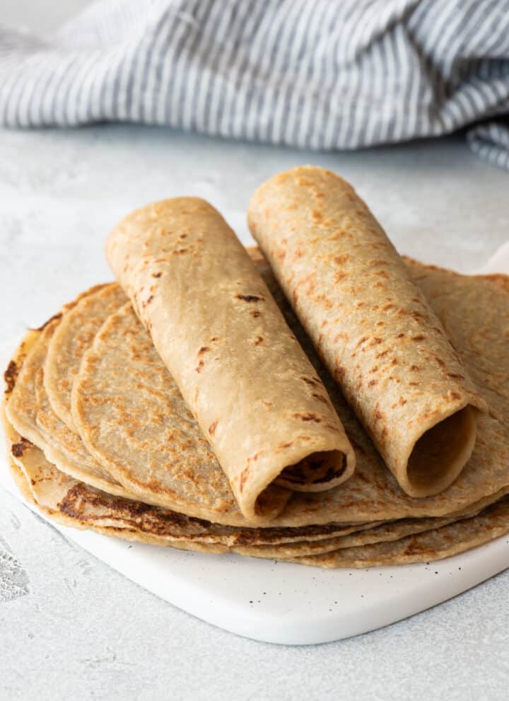 two quinoa tortillas rolled up on top of flat tortillas on gray background